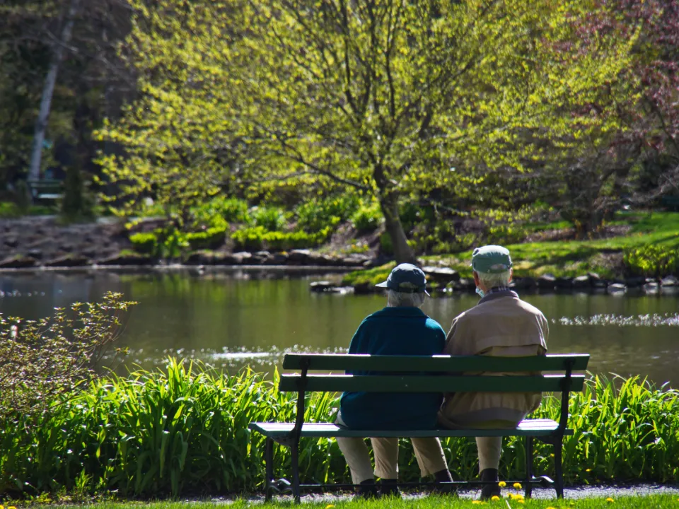 An older couple sitting together on a park bench beside a pond